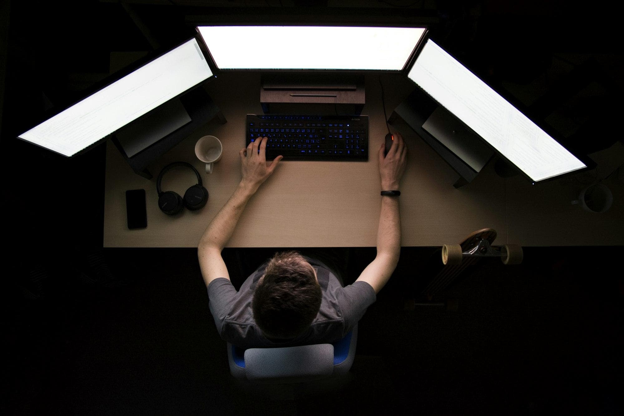 Developer at a desk with three monitors, seen from above in the dark